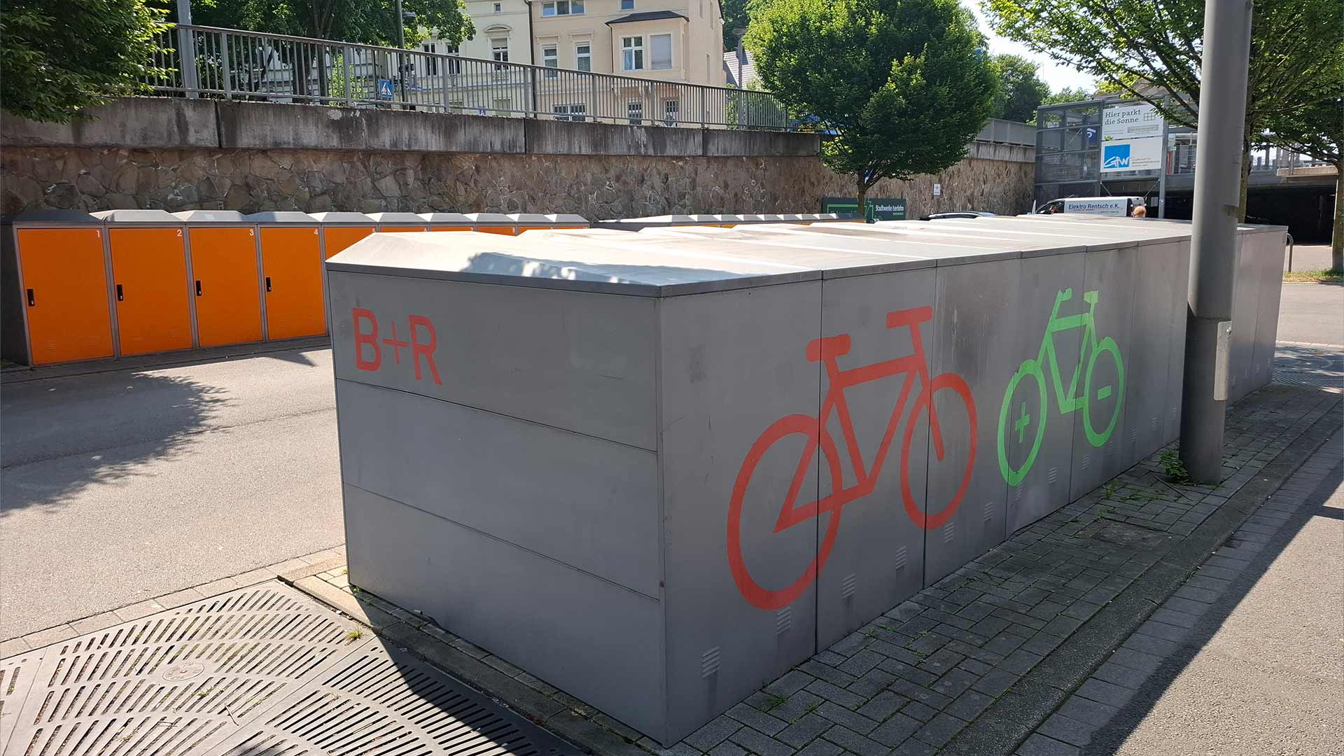 Fahrradboxen und B+R-Abstellanlage am Bahnhof Iserlohn, graue Container mit orange‑grünen Fahrradsymbolen, sichere Bike‑and‑Ride‑Infrastruktur