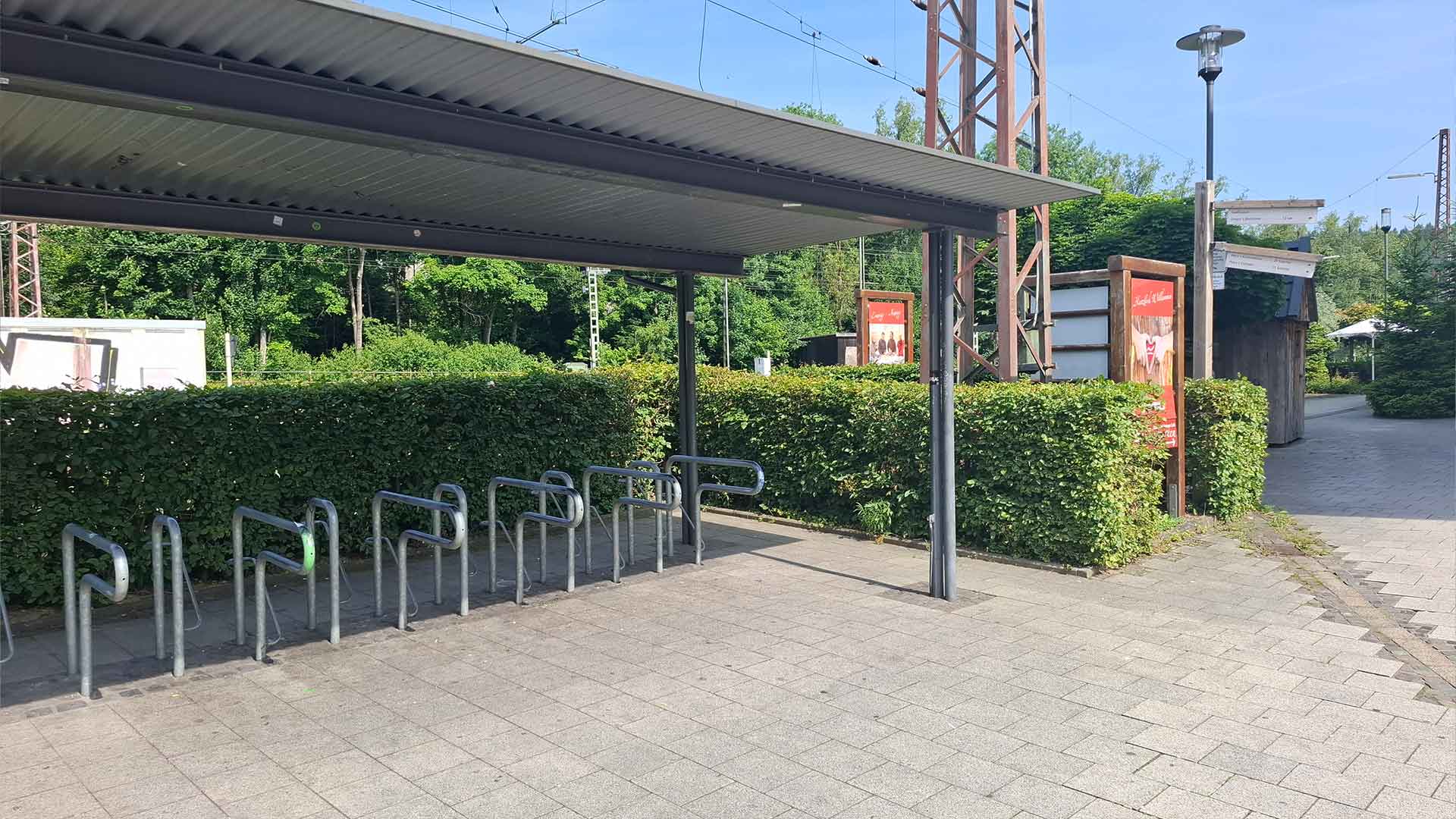 Überdachte Fahrradstellplätze am Bahnhof Lennestadt‑Altenhundem, Metallbügel neben Hecke, ruhiger Bereich unter freiem Himmel