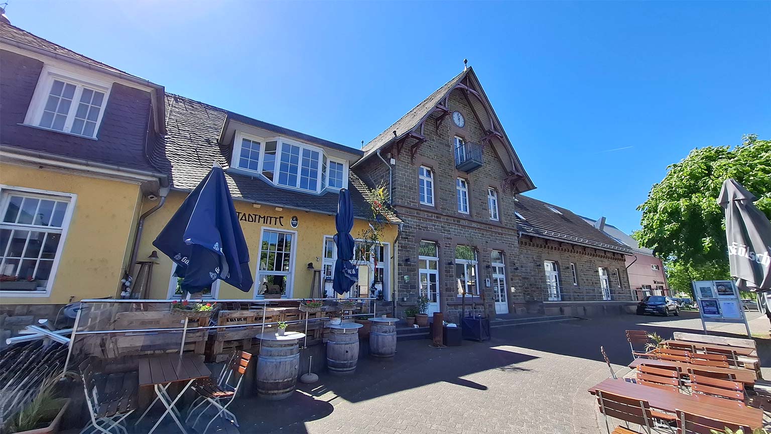 Historisches Bahnhofsgebäude Overath mit Außengastronomie und Biergartenmöbeln, blauer Himmel und gemütliche Atmosphäre an der Stadtmitte
