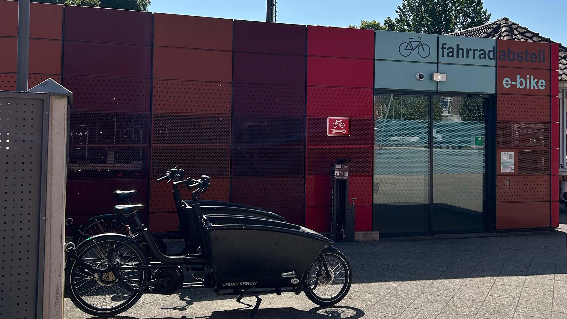 Fahrradabstellanlage am Bahnhof Detmold für E‑Bikes, moderne rot‑türkisfarbene Fassade, davor Lastenräder von Urban Arrow