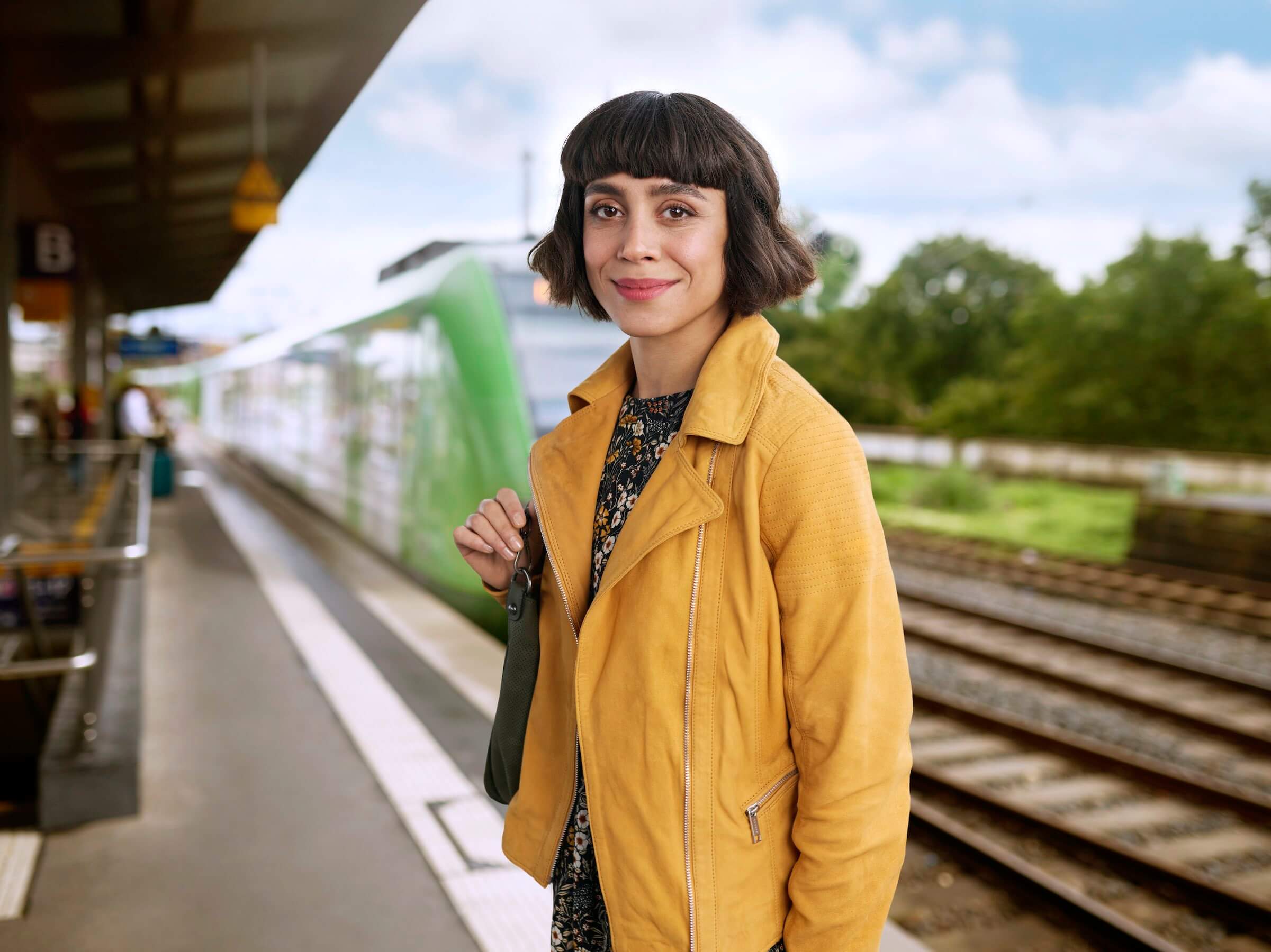 Eine Frau steht lächelnd am Bahngleis, hinter ihr ist eine S-Bahn