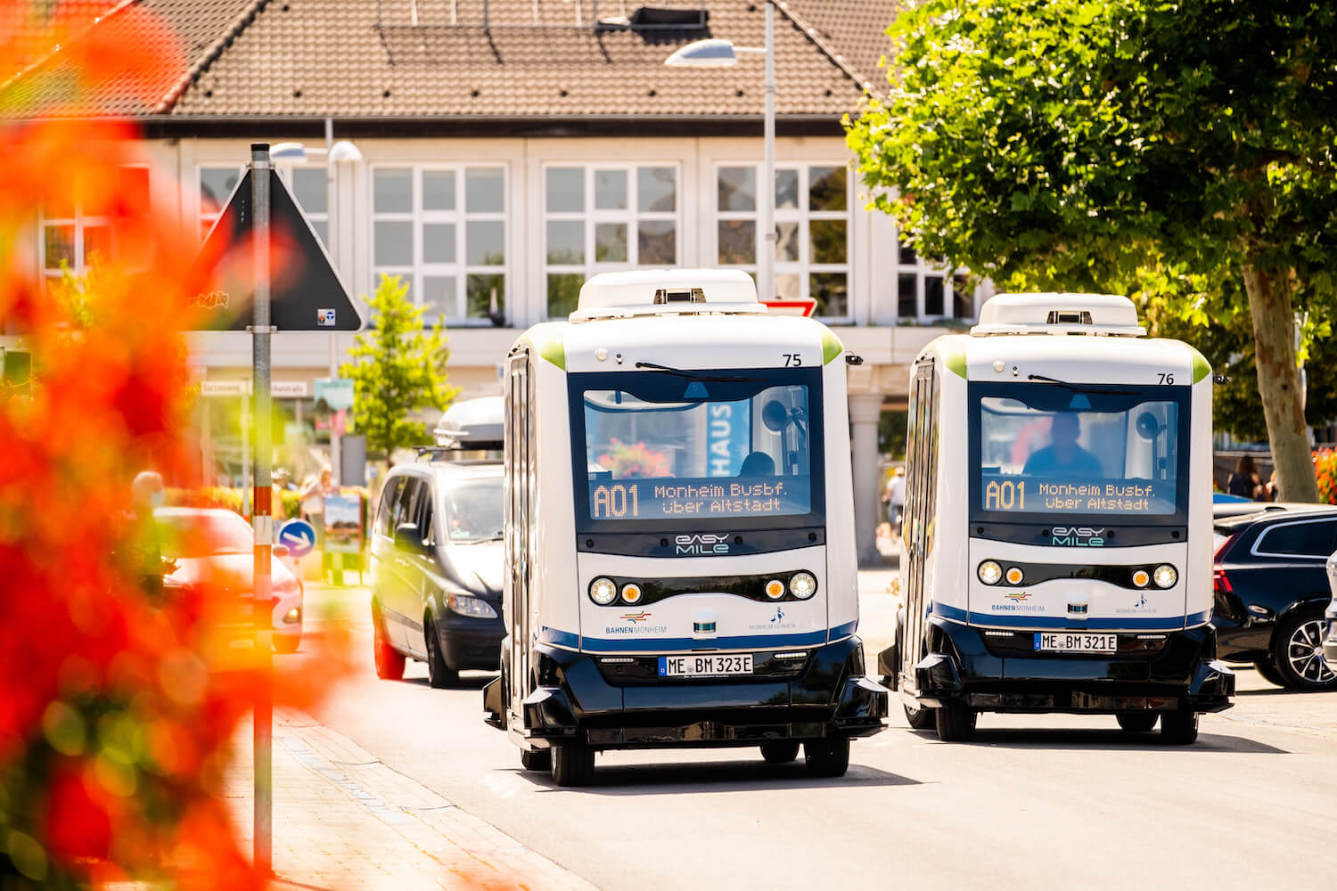 Zwei autonome Kleinbusse fahren nebeneinander auf einer Straße.