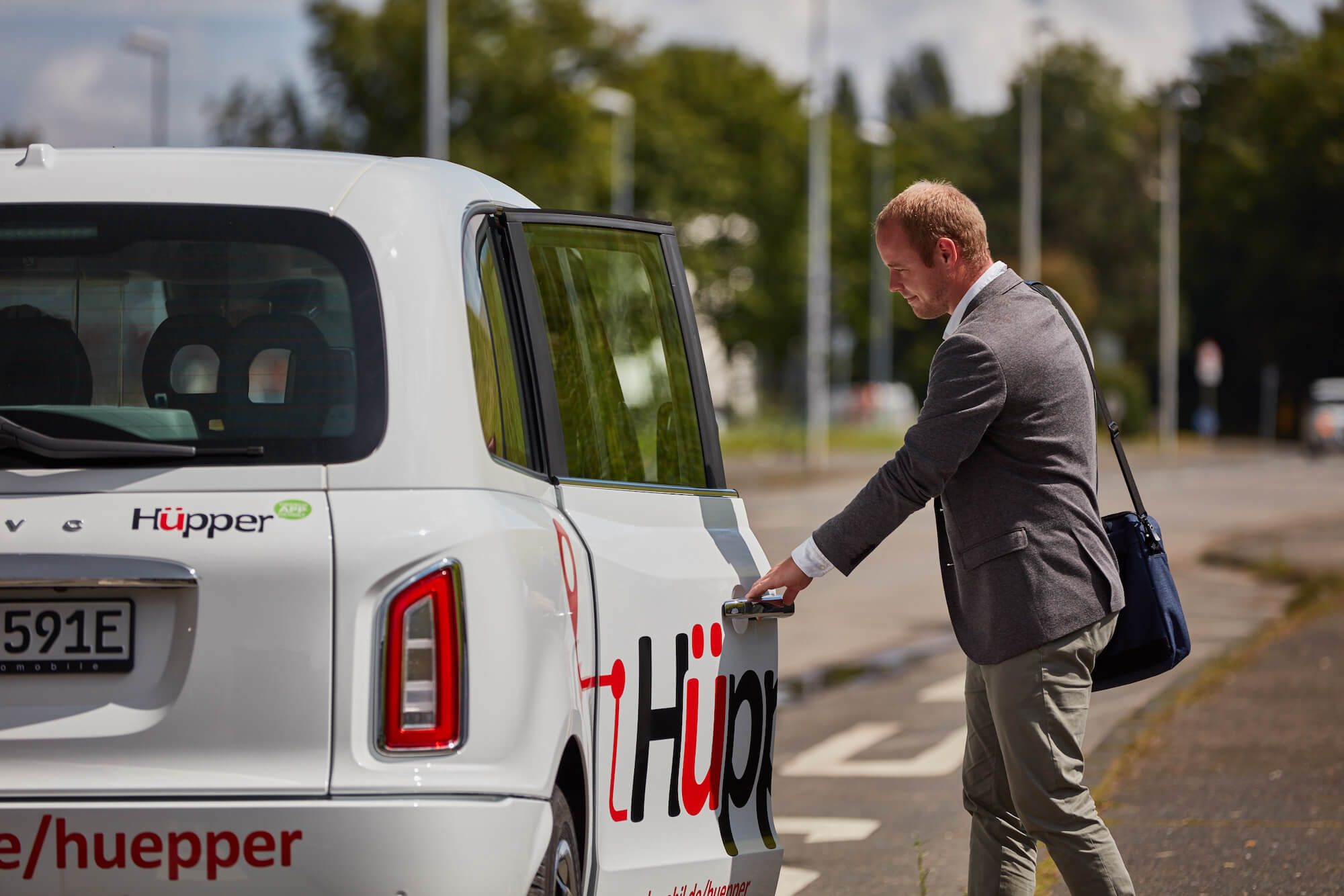 Mann geht auf ein weißes On-Demand-Auto zu und greift nach dem Türgriff.