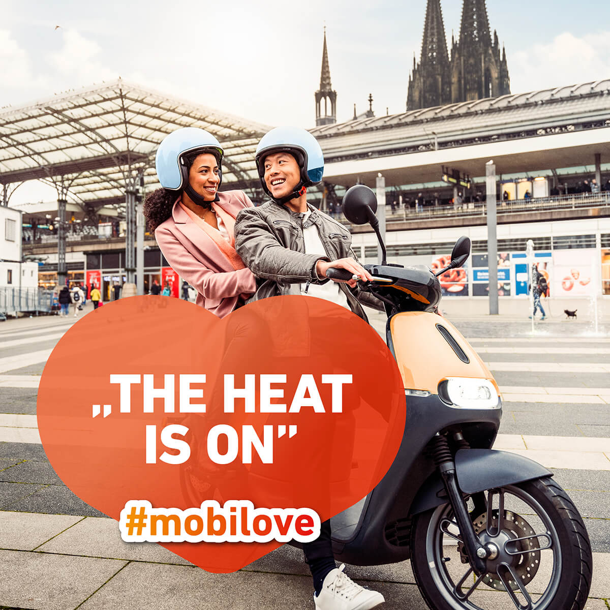 Mobilove-Visual: Ein Mann und eine Frau sitzen auf einem E-Roller, im Hintergrund ist der Kölner Dom. Herzchen-Kommentarblase: "The heat is on"