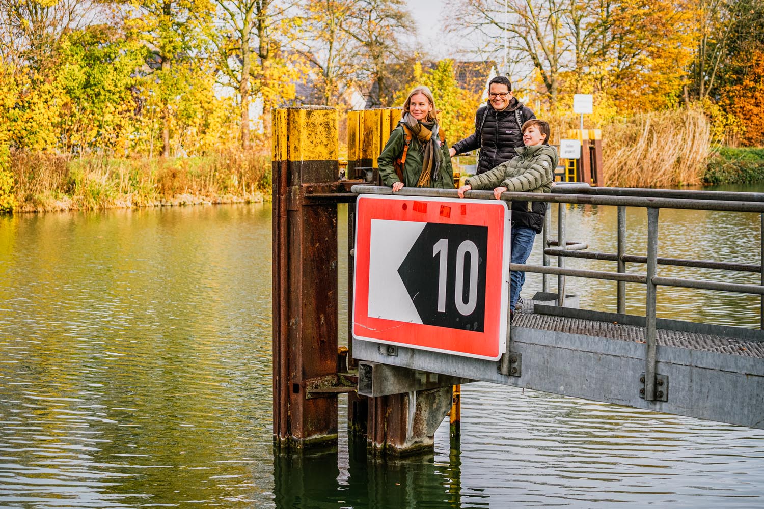 Eine Familie mit Mutter, Vater, Sohn steht auf einem Metallsteg über einem Fluss.