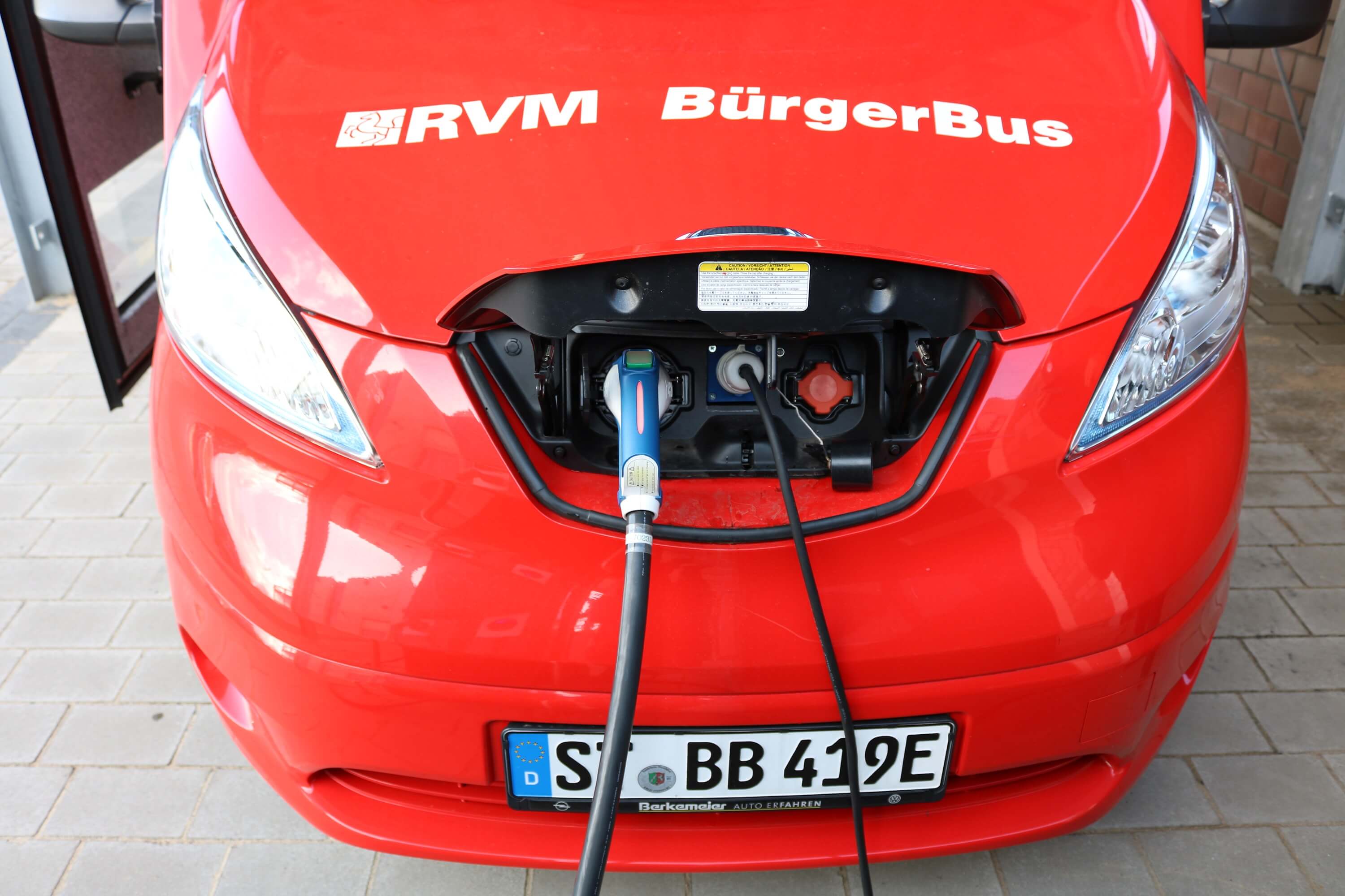 Der E-Bus des Bürgerbusvereins Emsdetten Sarbeck wird geladen. Man sieht nur die Motorhaube des roten Kleinbusses.