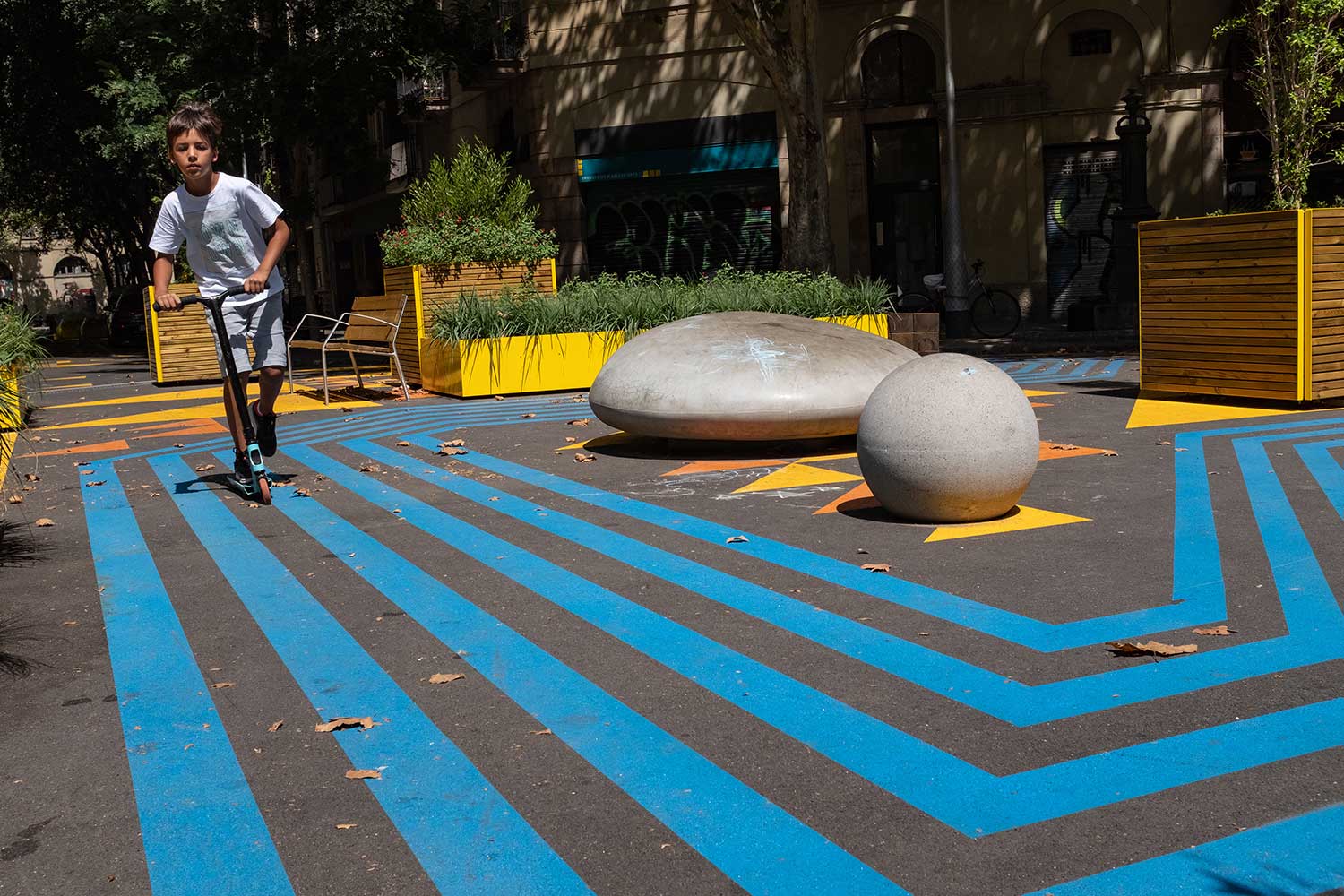Ein kleiner Junge fährt mit einem Tretroller über den bunt angemalten Boden in einem Superblock in Barcelona.
