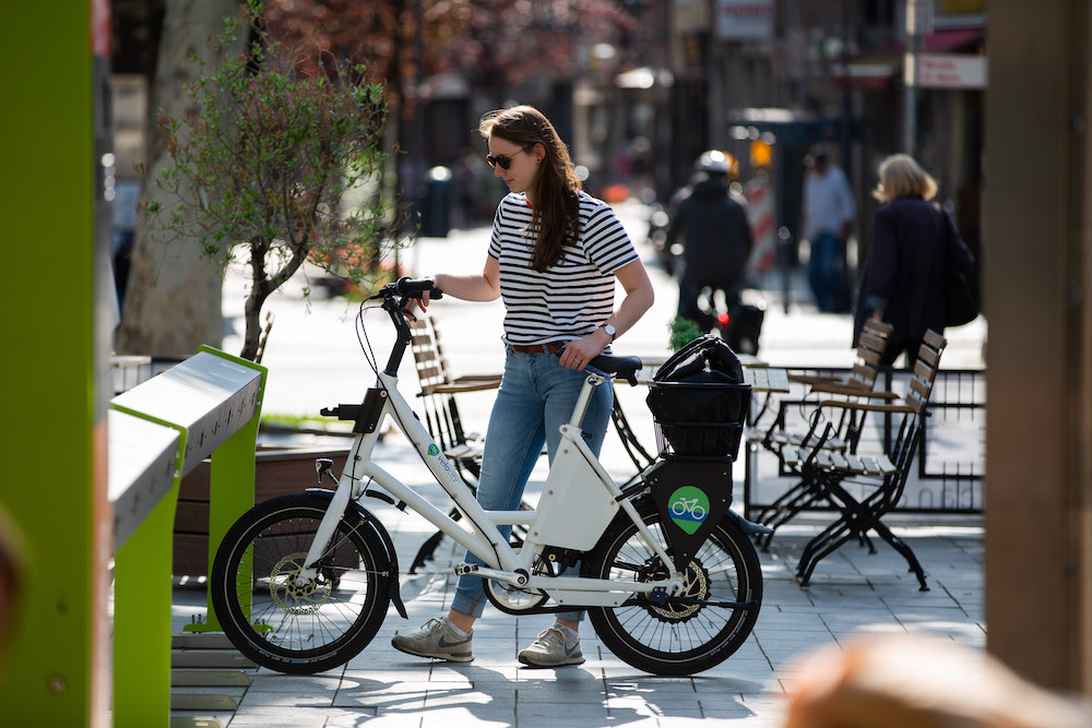 Eine junge Frau schiebt ein E-Bike aus einer Fahrradverleihstation.
