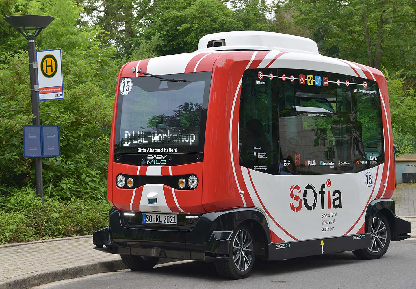 Ein kleiner rot-weißer Shuttlebus steht an einer Bushaltestelle.