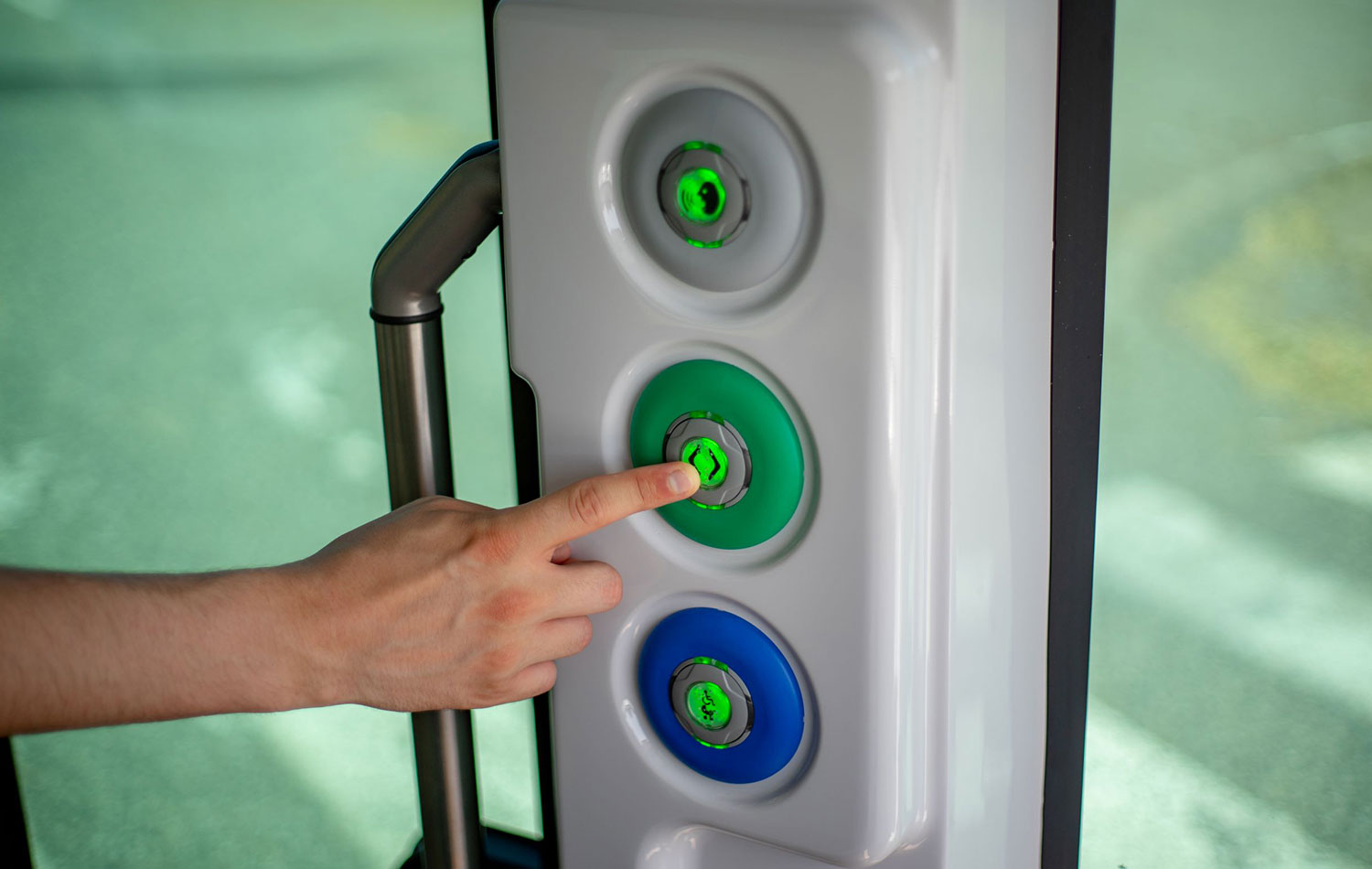 Eine Hand drückt auf einen grünen Türöffnerknopf in einem Shuttlebus.