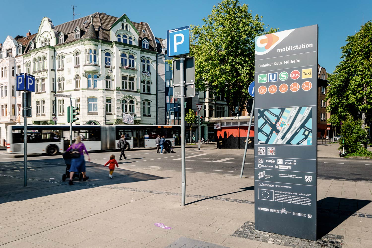 Die Stele der Mobilstation am Bahnhof Köln-Mülheim. Im Hintergrund fährt ein Bus vorbei.