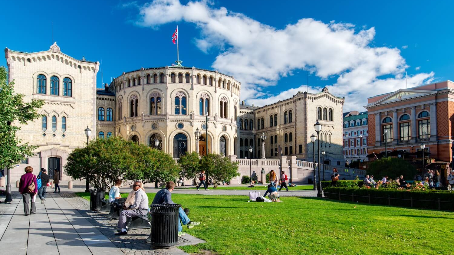 Der Platz vor dem norwegischen Parlament bei sommerlichem Wetter. Viele Menschen sitzen auf Bänken.