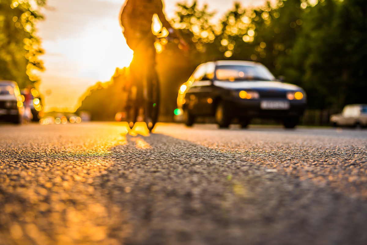 Ein Auto und ein Fahrrad fahren im Sonnenuntergang nebeneinander auf einer von Bäumen gesäumten Straße.
