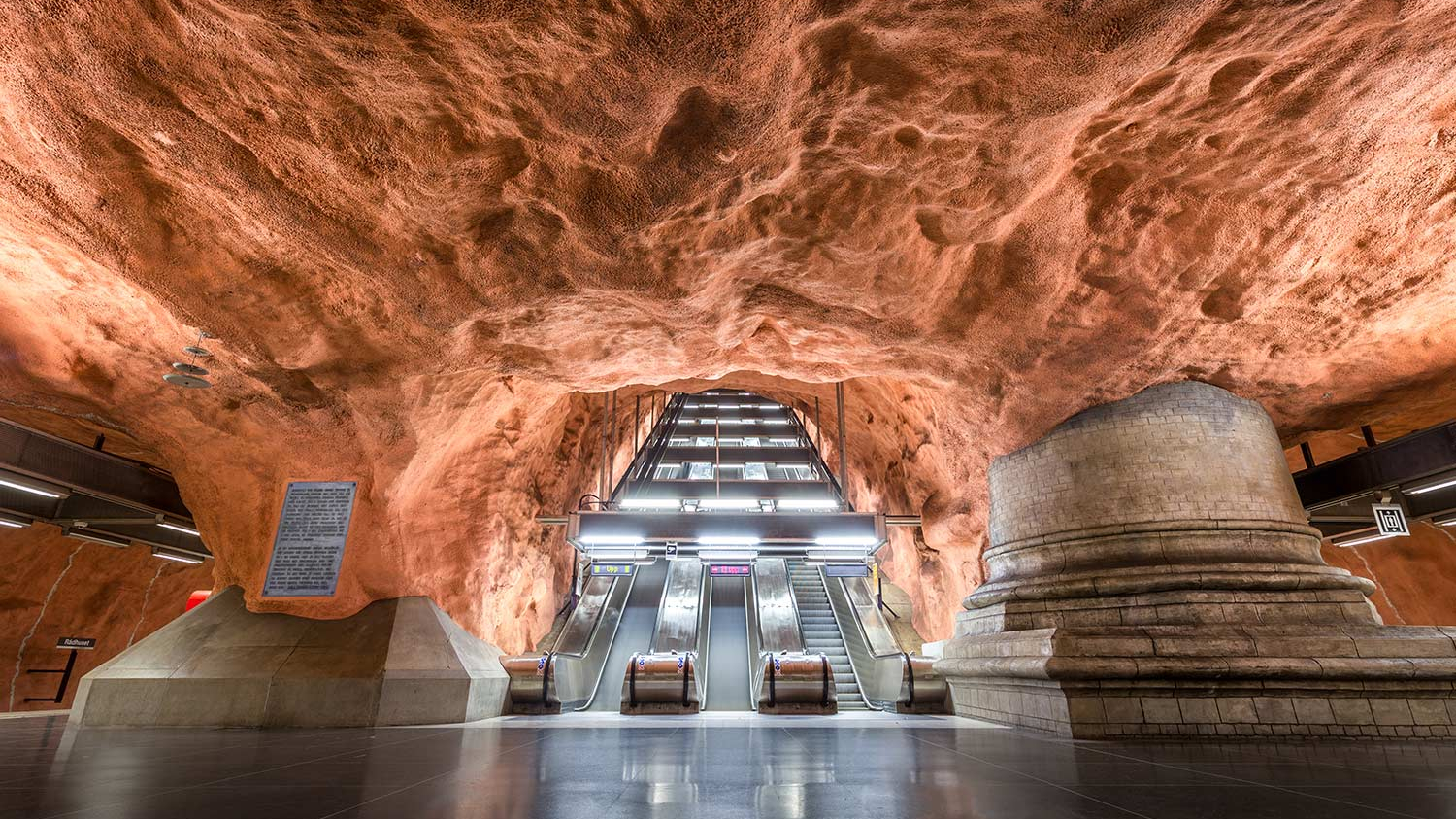 Rolltreppen in einer Stockholmer U-Bahn-Station, deren Decke wie eine Sandsteinhöhle gestaltet ist.