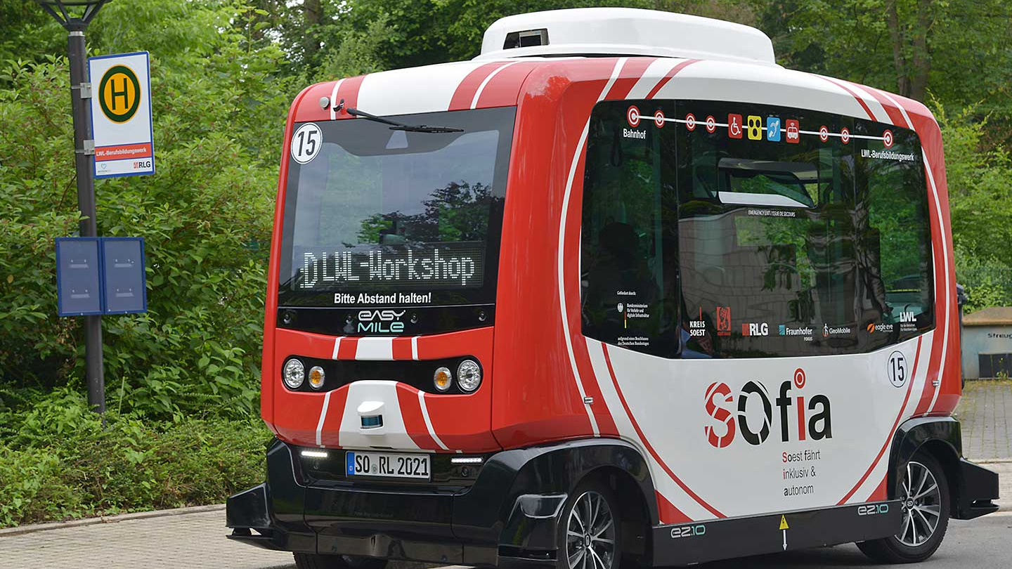 Ein kleiner rot-weißer Shuttlebus steht an einer Bushaltestelle.