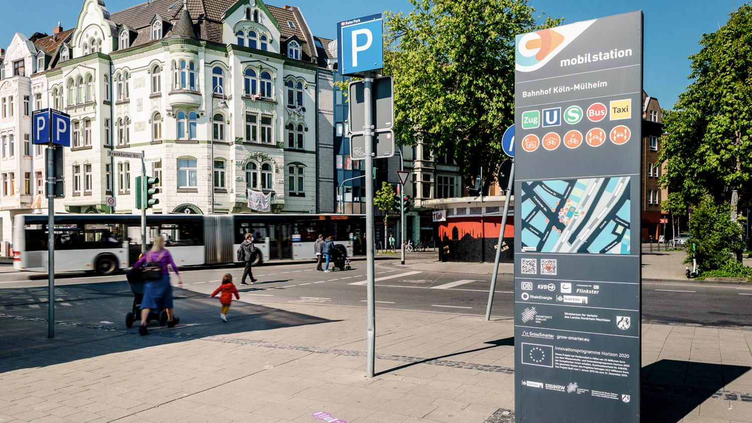 Die Stele der Mobilstation am Bahnhof Köln-Mülheim. Im Hintergrund fährt ein Bus vorbei.