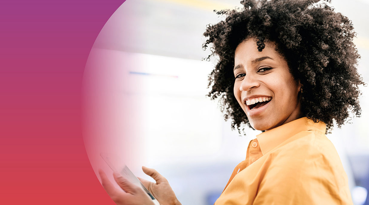 Eine junge Frau hält in der Bahn ein Handy in der Hand und lacht in die Kamera.