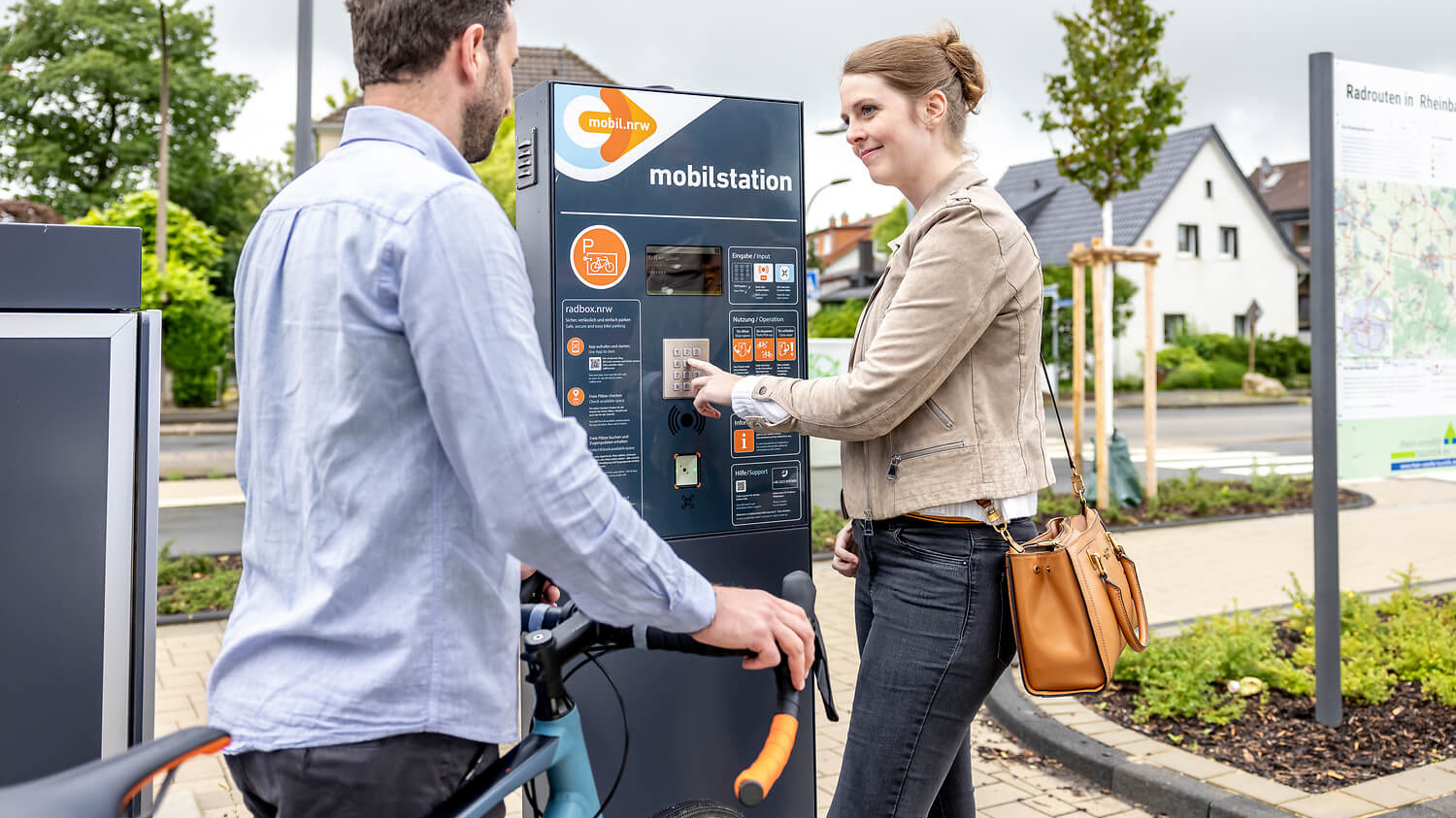 Zu sehen sind zwei Menschen welche an einem Informationsterminal stehen.