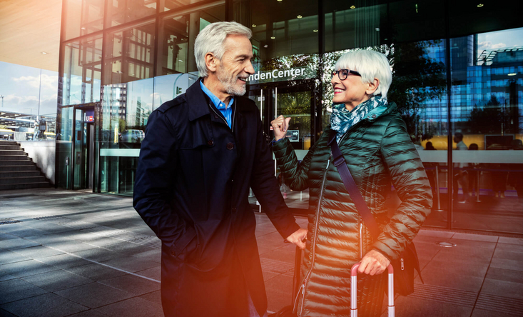 Ein älteres Ehepaar steht mit Koffern vor einem DB Servicecenter.