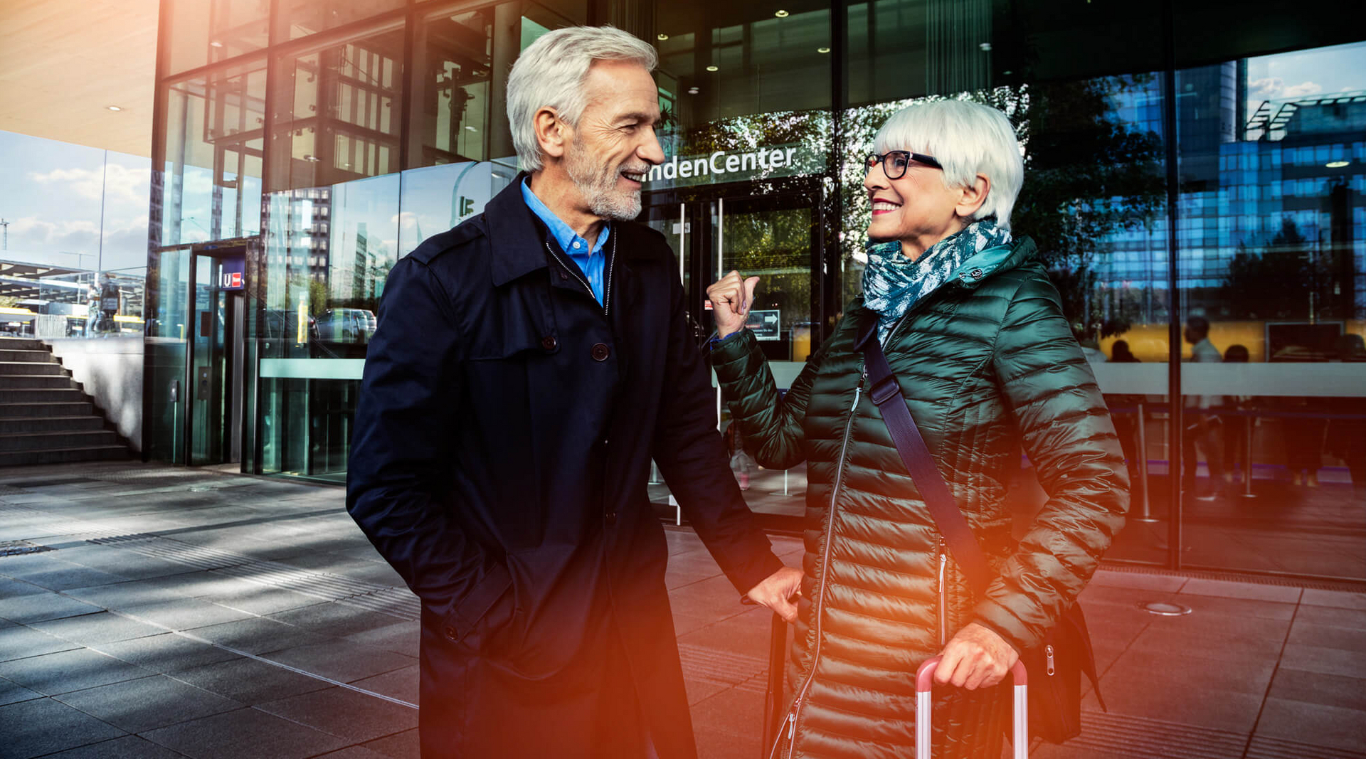Ein älteres Ehepaar steht mit Koffern vor einem DB Servicecenter.