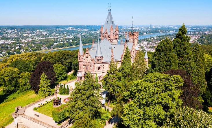 Das malerische Schloss Drachenburg liegt in einer strahlenden sommerlichen Naturlandschaft.