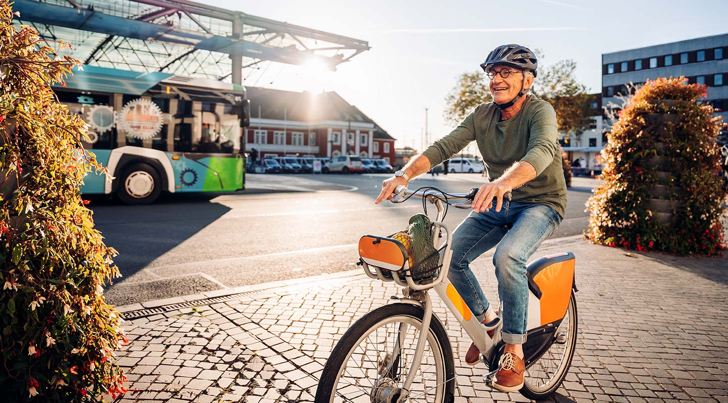 Ein Senior fährt auf einem Fahrrad an einem Busbahnhof vorbei.
