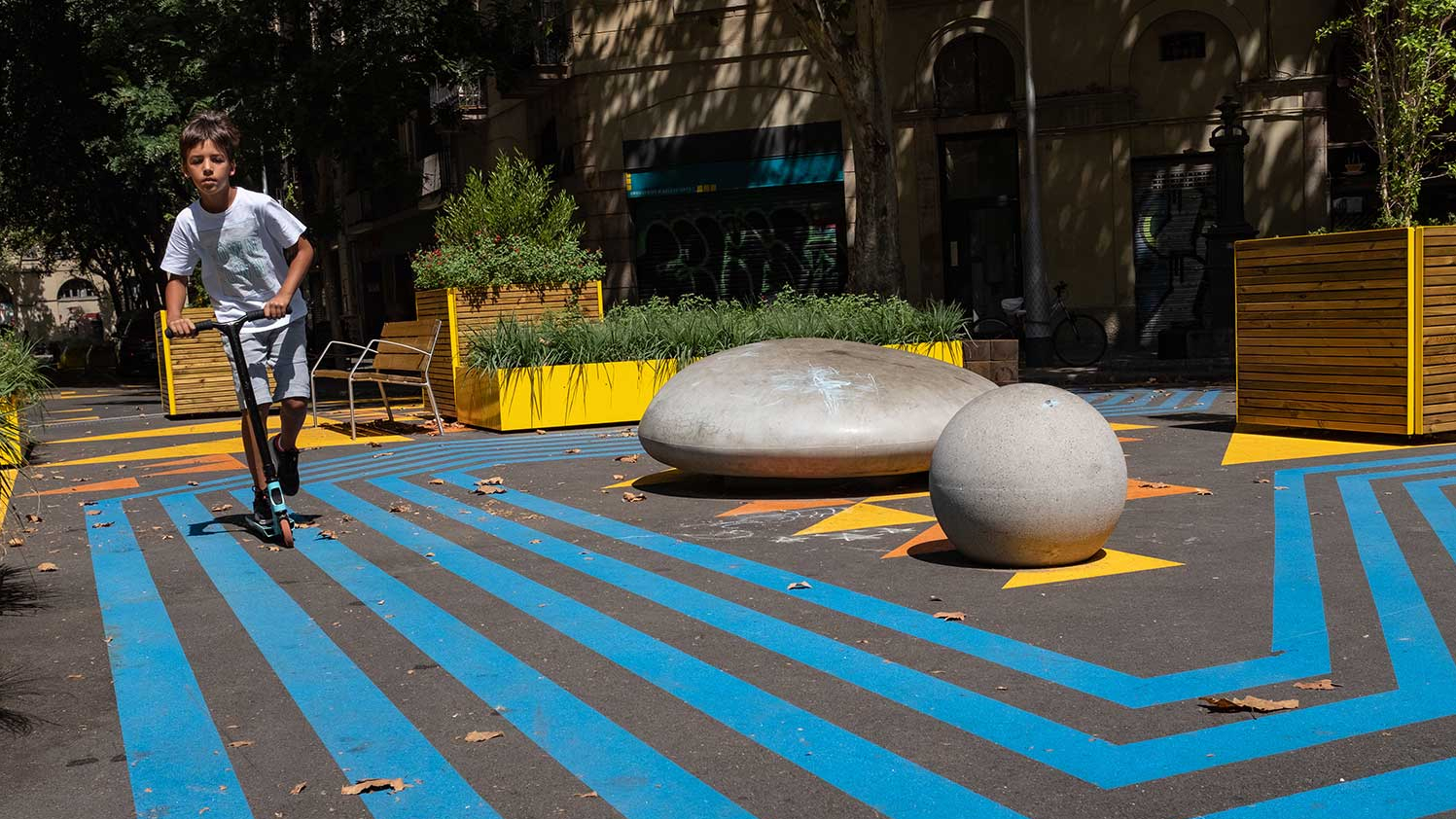 Ein kleiner Junge fährt mit einem Tretroller über den bunt angemalten Boden in einem Superblock in Barcelona.