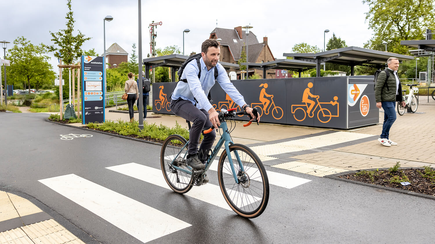 Zu sehen ist ein Mann der ein Fahrrad fährt. Im Hintergrund sind Fahrradboxen zu sehen. 