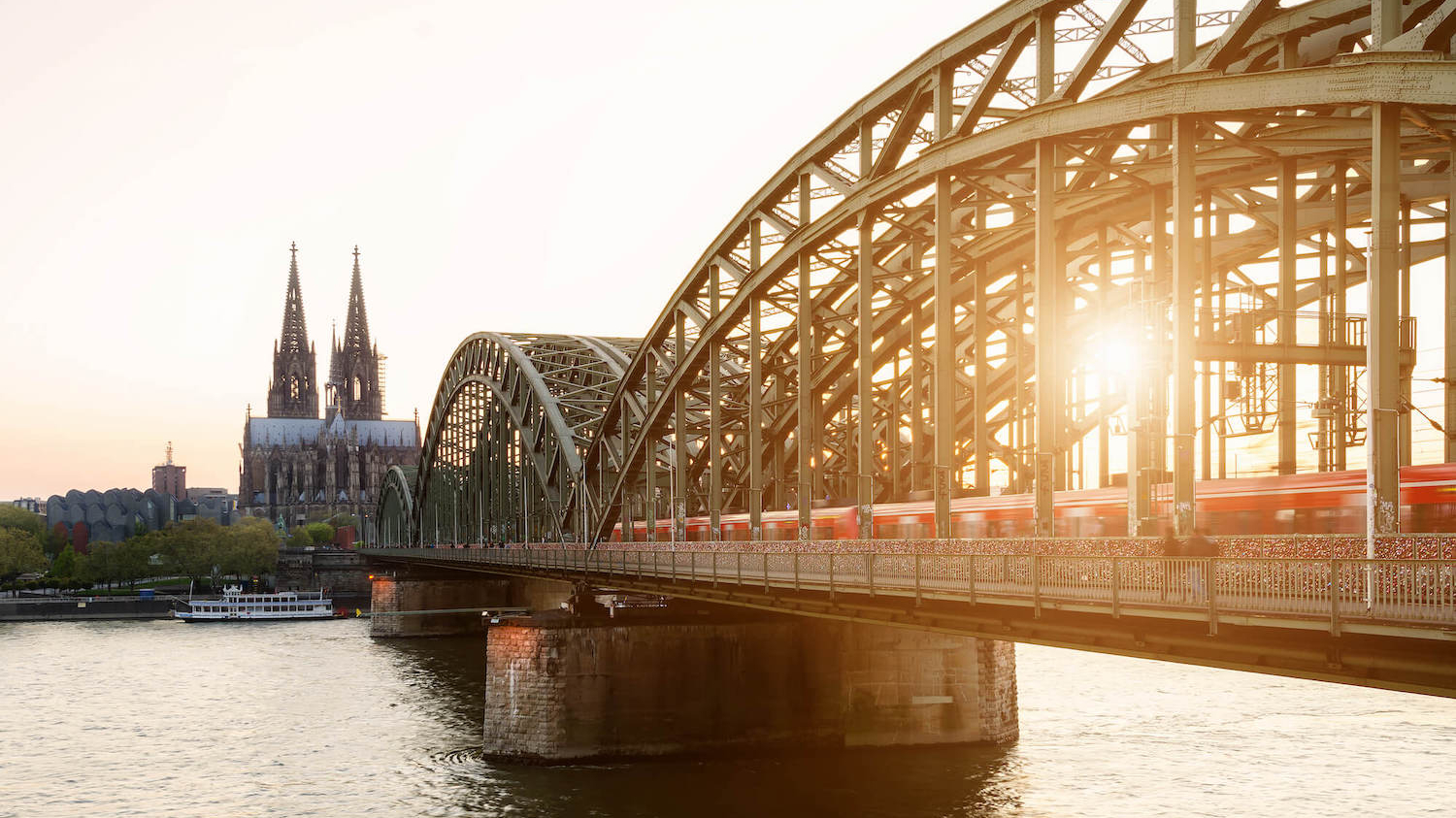 Eine S-Bahn fährt im Sonnenuntergang über die Hohenzollernbrücke in Köln, im Hintergrund der Kölner Dom.