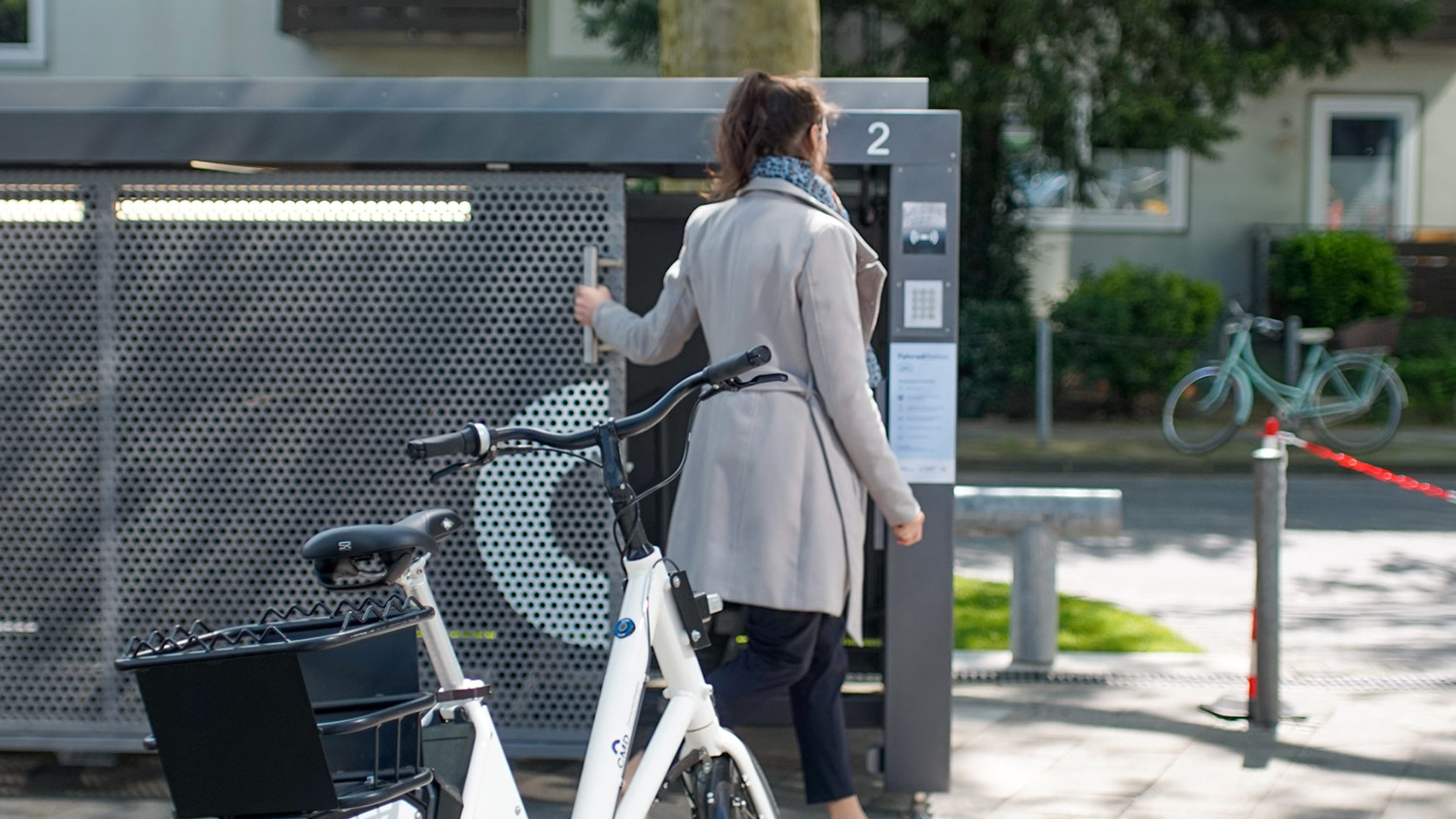 Eine Frau hat ein Fahrrad aus einer Radbox geholt und schließt die Tür der Box.