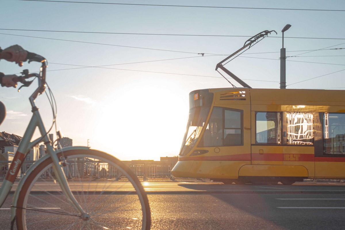 Ein halb sichtbares Fahrrad und eine halb sichtbare Straßenbahn in entgegengesetzter Richtung. Im Hintergrund sieht man den Sonnenuntergang.