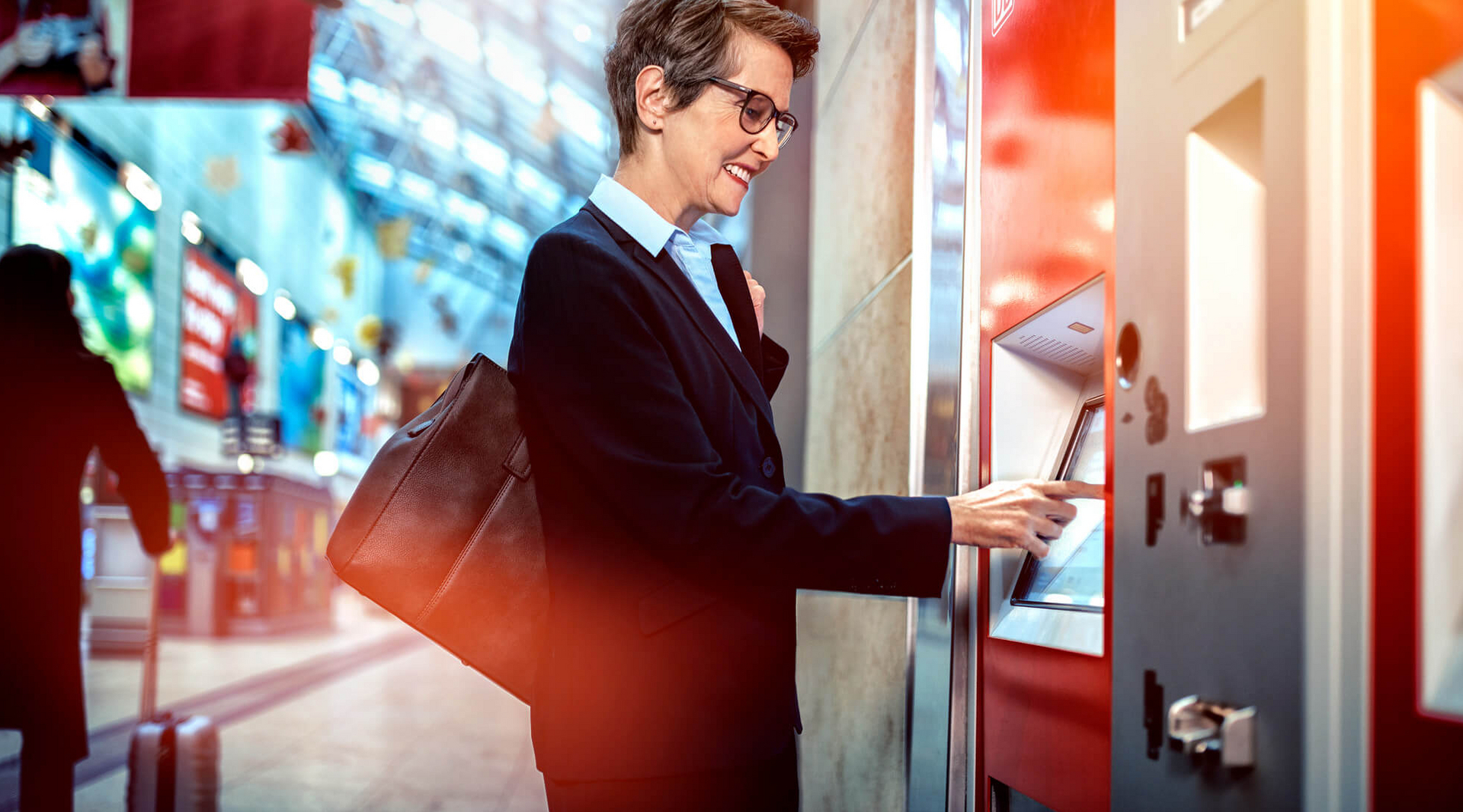 Eine Frau steht vor einem Fahrkartenautomat und tippt auf den Touchscreen.