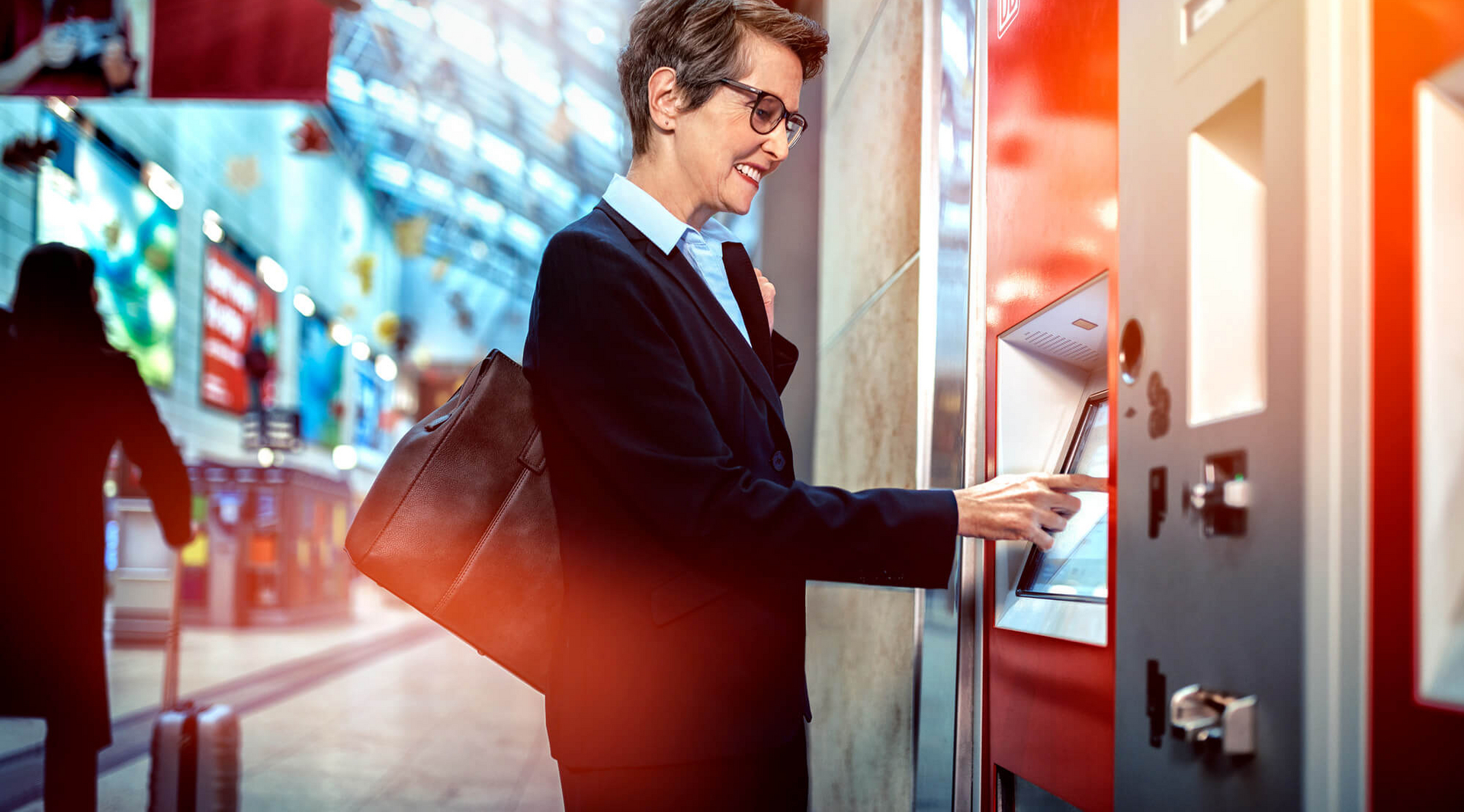 Eine Frau steht vor einem Fahrkartenautomat und tippt auf den Touchscreen.