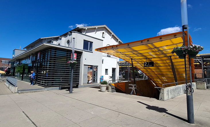 Bahnhof Emsdetten mit moderner, gelber Überdachung zum Zugang Gleis 2, weißes Empfangsgebäude und blauer Himmel