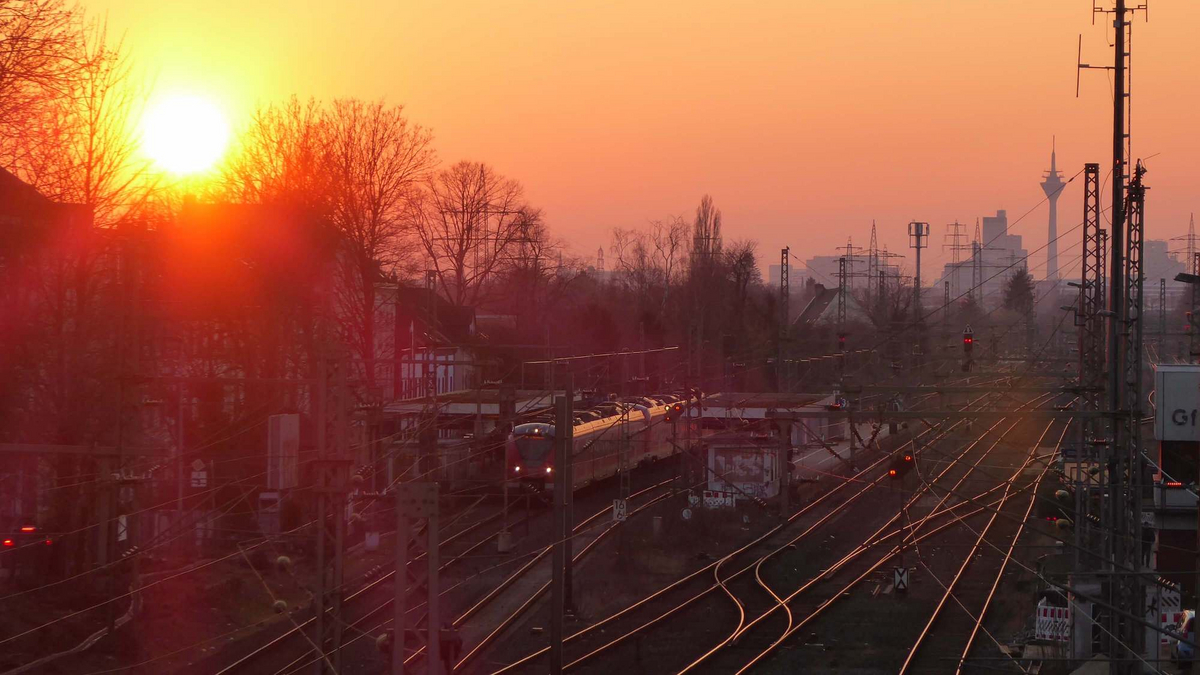 Blick auf die Schinen des Bahnhofs und die Düsseldorfer Innenstadt, ausgehend vom Bahnhof Düsseldorf-Gerresheim im Sonnenuntergang