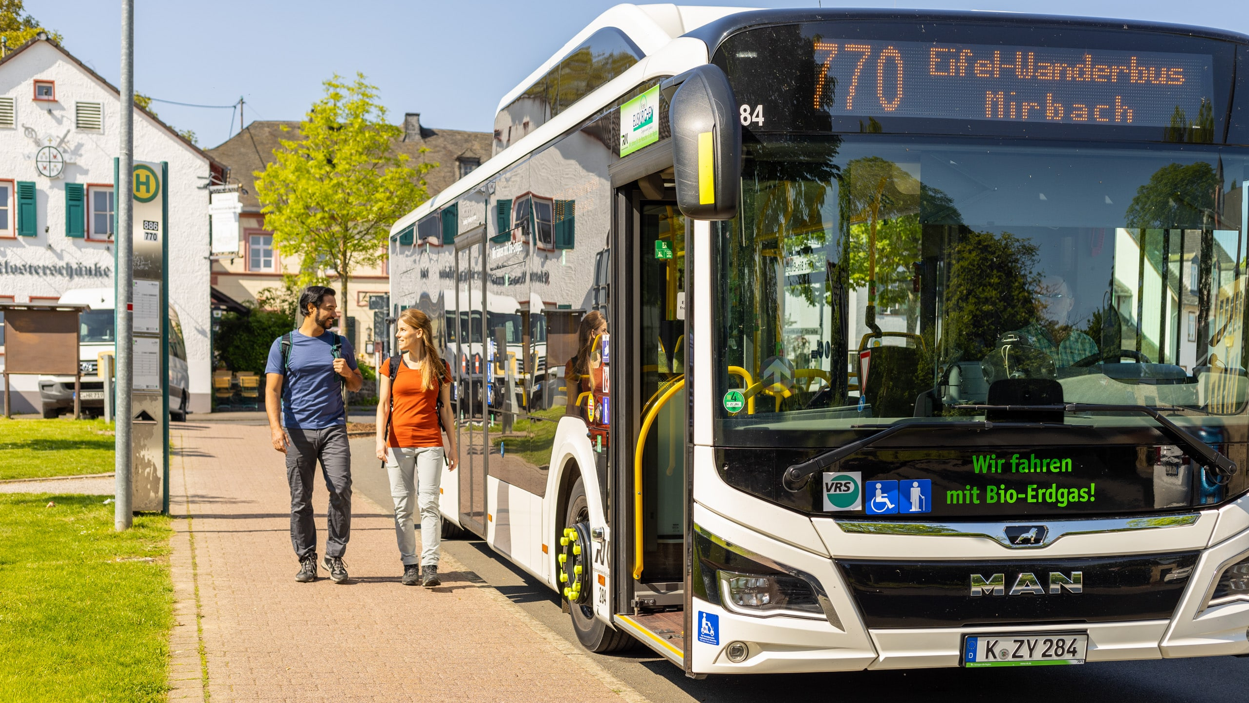 Zwei Wander:innen laufen an einem Bus vorbei.