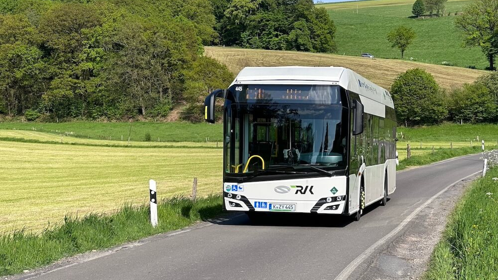 Ein Wasserstoffbus fährt durch grüne Landschaft.