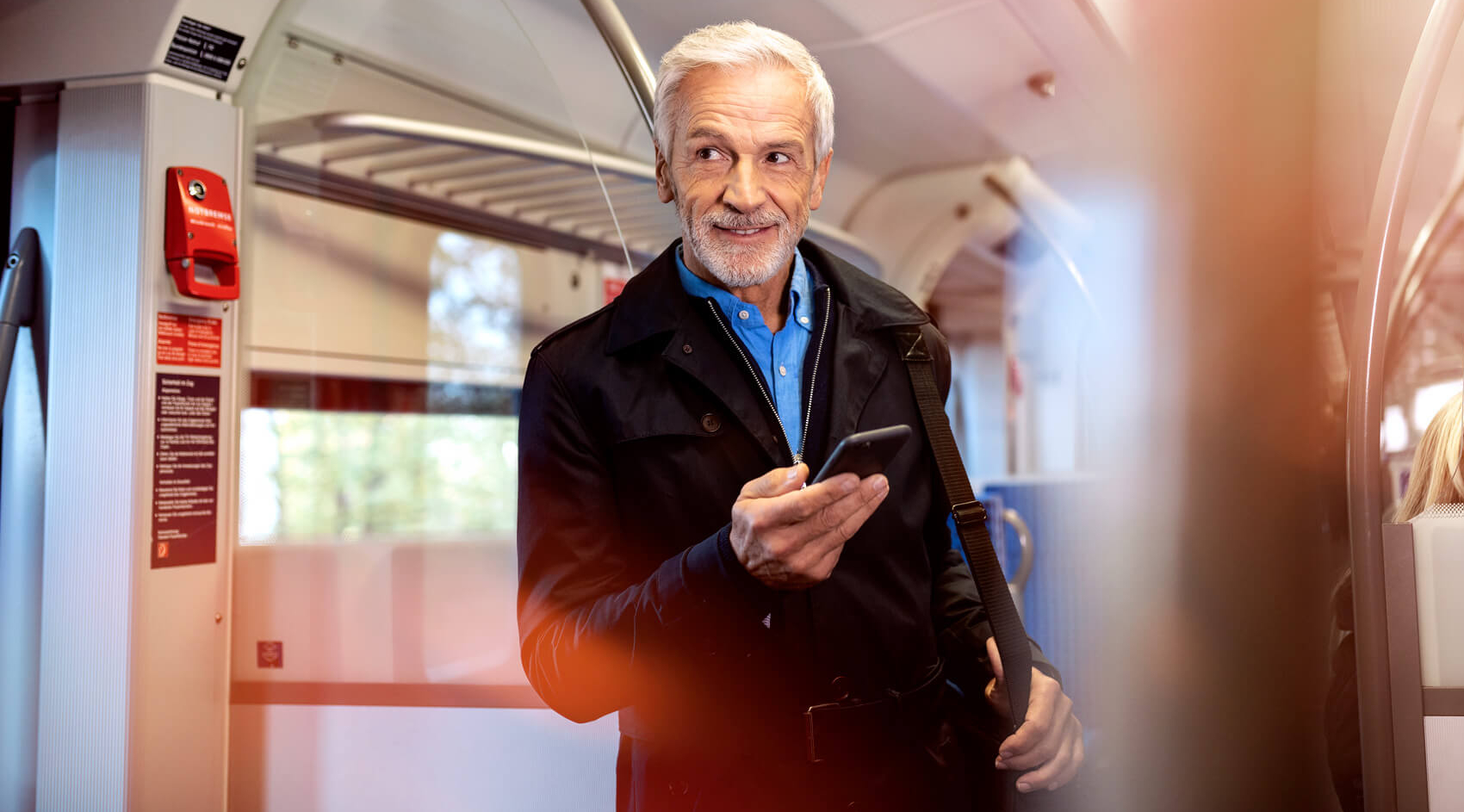 Ein älterer Mann steht mit einem Handy in der Hand in einem Bus.