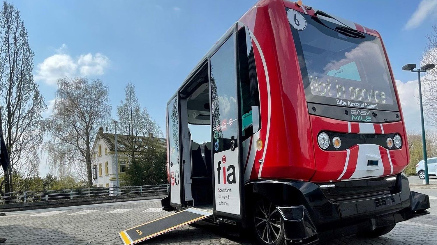 Ein kleiner rot-weißer Shuttlebus steht auf einem Platz und hat eine Rampe für Rollstuhlfahrer ausgeklappt.