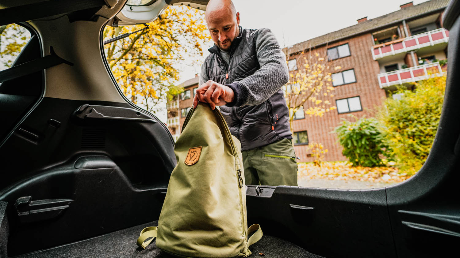 Ein Mann schaut in den Kofferraum eines Autos und stellt dort einen Rucksack ab.