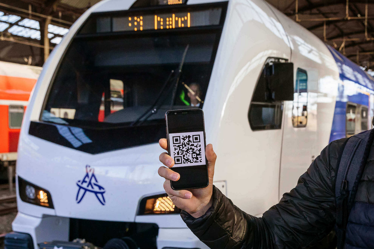 Eine Person hält ein Handy vor einem Zug in der Hand. Auf dem Handybildschirm ist ein QR-Code zu sehen.