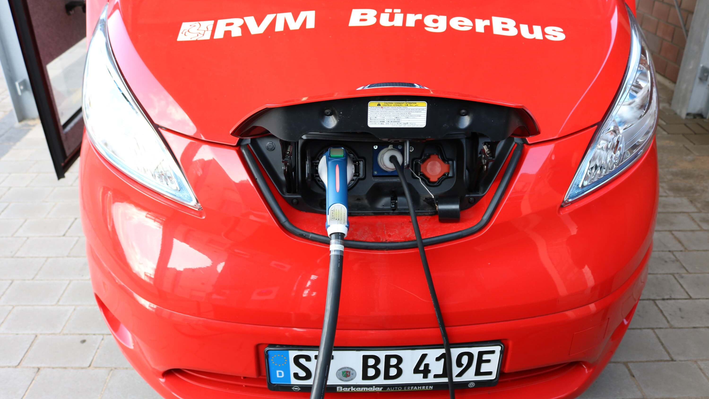 Der E-Bus des Bürgerbusvereins Emsdetten Sarbeck wird geladen. Man sieht nur die Motorhaube des roten Kleinbusses.