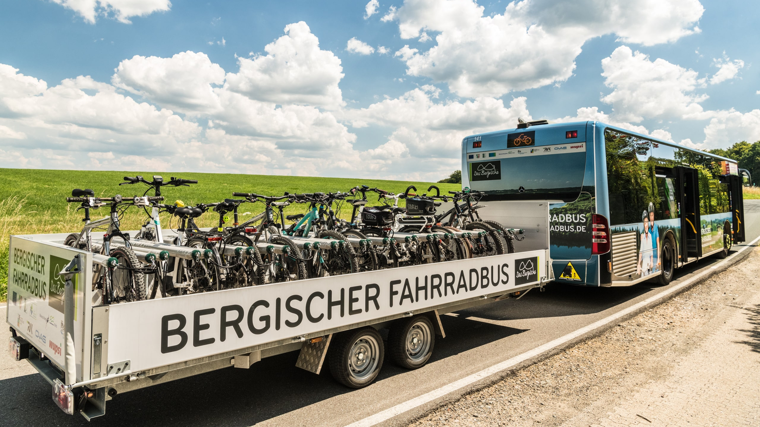 Ein Bus steht mit einem vollen Fahrradanhänger mit der Aufschrift "Bergischer Fahrradbus" an einer Straße.