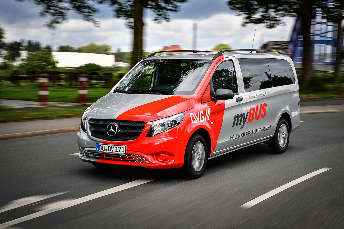 Ein rot-silberner Kleinbus mit dem Aufdruck myBUS fährt schnell auf einer Straße in der Stadt.