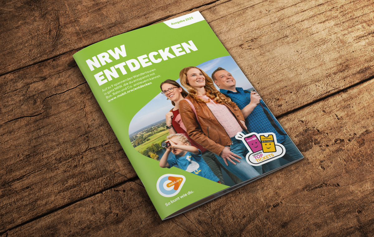 Zu sehen ist eine Grafik, welche den Wanderfolder von NRW Entdecken 2025 auf einer Holzplatte zeigt. 