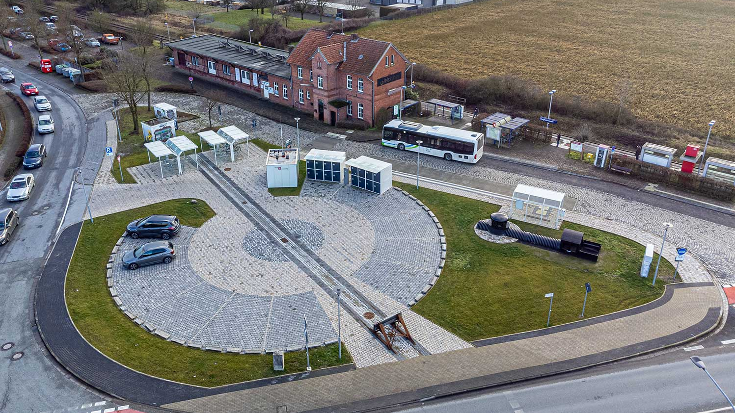 Luftaufnahme der Mobilstation am Bahnhof Borgholzausen mit Blick auf die Gleise, einen Bus und den Platz für E-Autos.