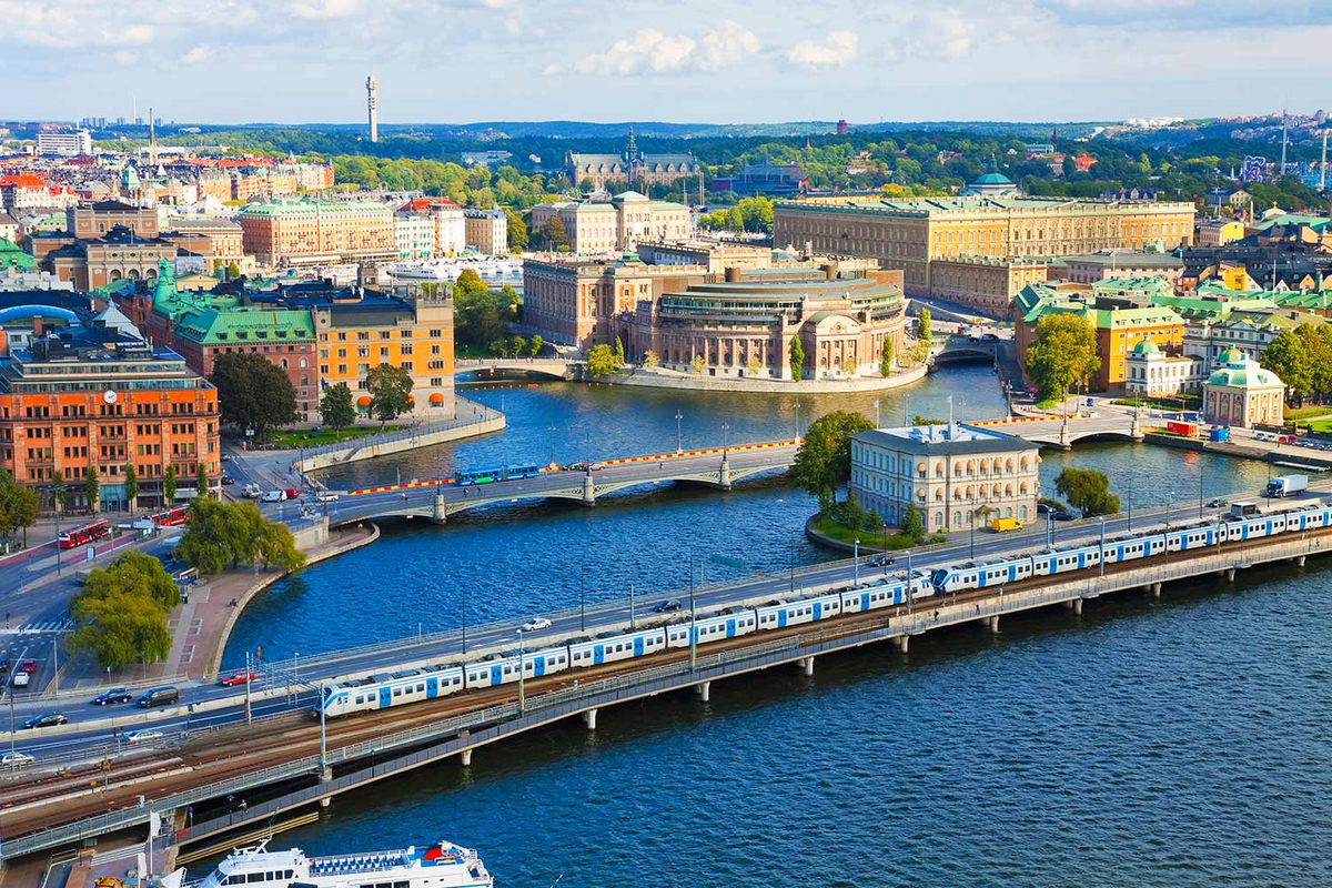 Luftbild von Stockholm mit Blick auf Schienen, die über einen Fluss führen. Auf den Schienen fahren blaue Züge.