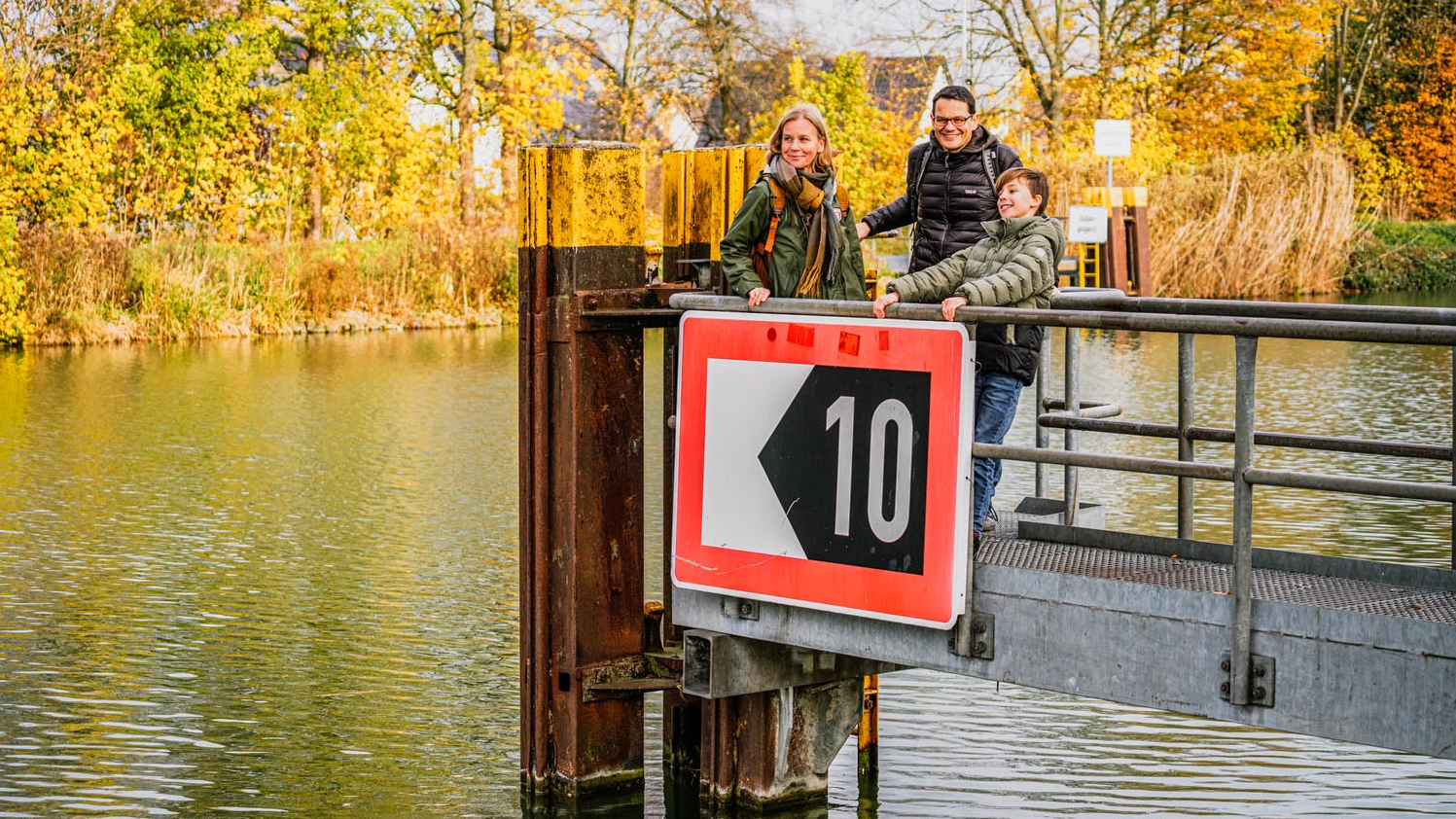 Eine Familie mit Mutter, Vater, Sohn steht auf einem Metallsteg über einem Fluss.