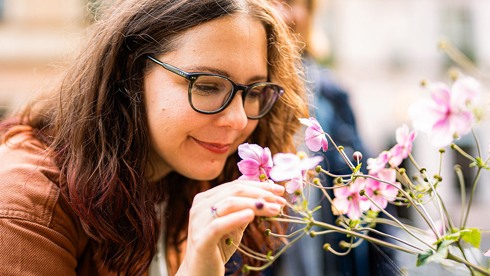 Zu sehen ist eine Frau, welche an Blumen riecht. 