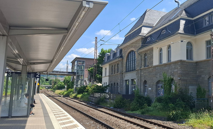 Historisches Bahnhofsgebäude Werdohl mit modernem Bahnsteig und Oberleitungen, sonniger Tag, Blick entlang der Gleise